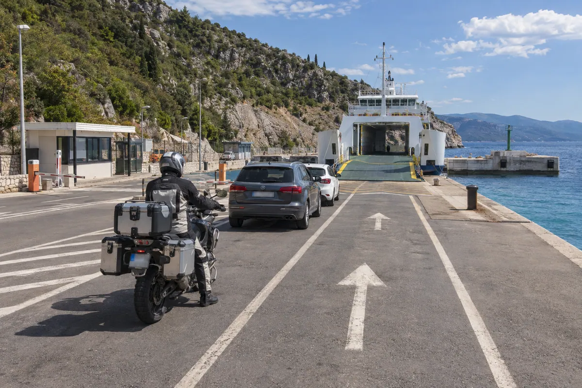 A touring motorcyclist waits in marked vehicle lanes facing the ferry ramp at Porozina port on Cres.