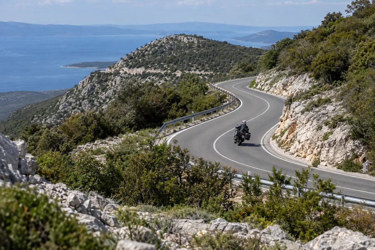 A motorcyclist follows successive D100 bends through rocky terrain above the Kvarner coast south of Porozina.
