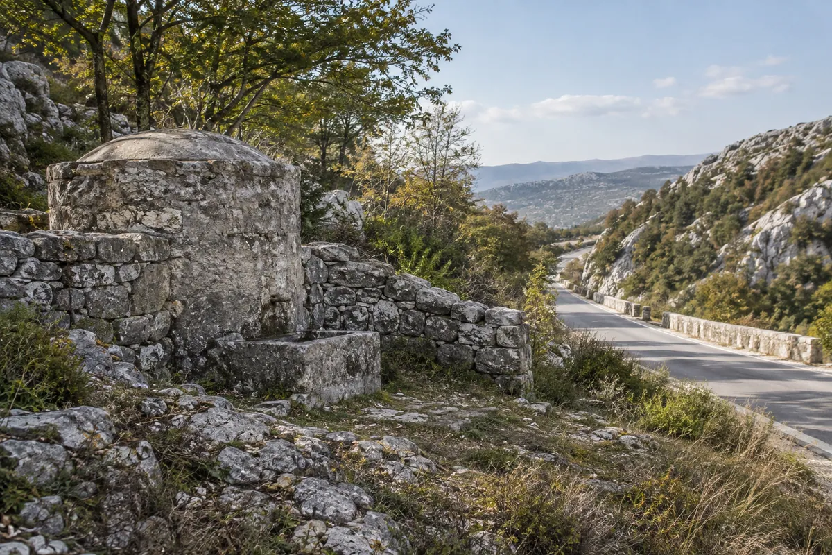 An old stone roadside water structure and low wall evoke the historic works near Kamenjak.