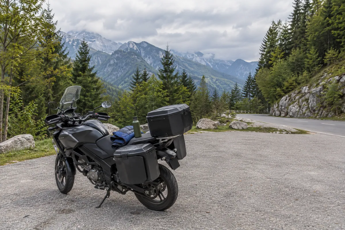 A parked touring motorcycle and rain gear illustrate preparation for changing Alpine weather.