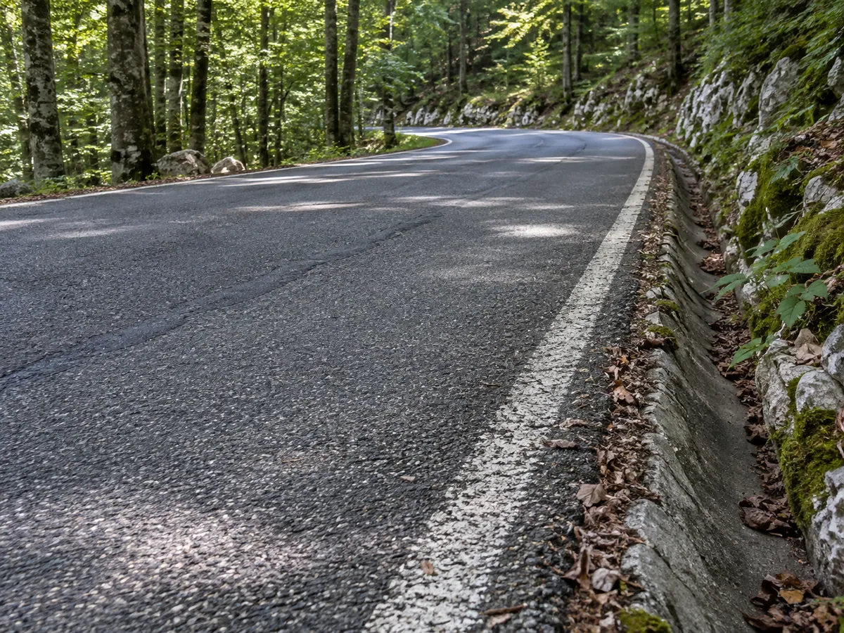 Shaded asphalt, a worn white edge line and a narrow drainage channel illustrate the Učka road surface.
