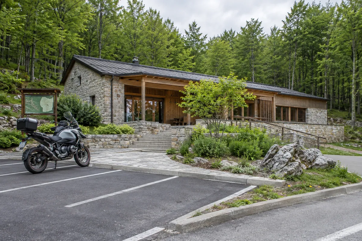 A touring motorcycle stands in marked parking beside a stone-and-timber interpretation of Poklon Visitor Centre.
